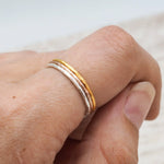 Hand wearing three hammered stacker rings on a light background