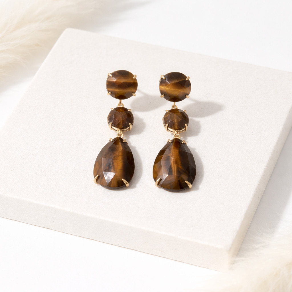 Pair of gold tigers eye teardrop earrings by Indie and Harper, on a white surface
