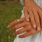 Close-up of a hand wearing a green blue natural tourmaline gemstone ring with a blurred grass background