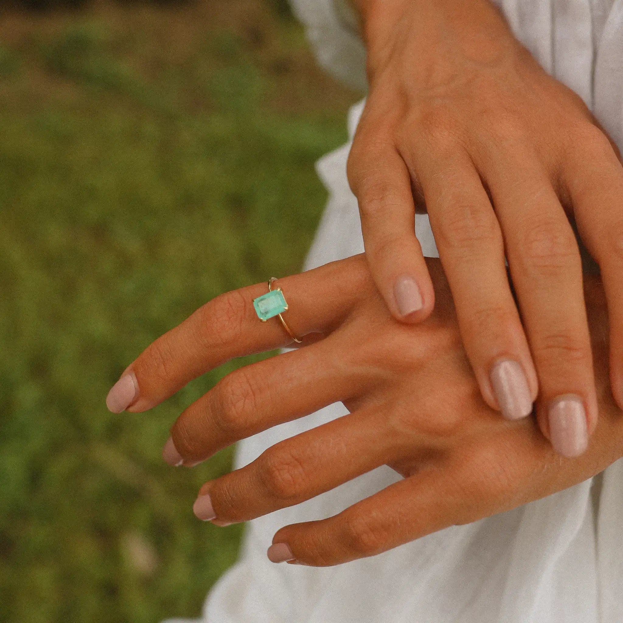 Close-up of a hand wearing a green blue natural tourmaline gemstone ring with a blurred grass background