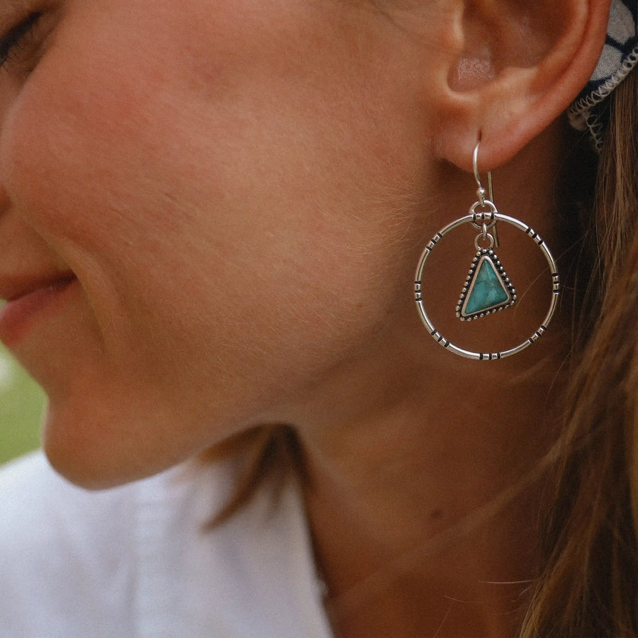 woman wearing sterling silver earrings with a hoop that has a triangular turquoise stone hanging in the middle