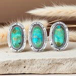 Three silver-framed turquoise stones on a wooden surface with dried grasses in the background.