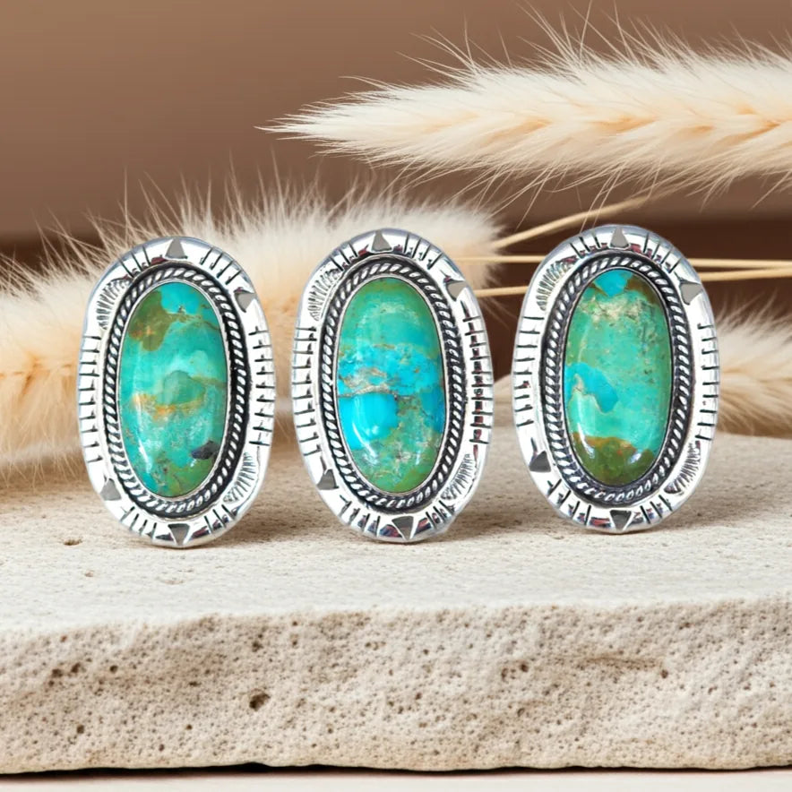 Three silver-framed turquoise stones on a wooden surface with dried grasses in the background.