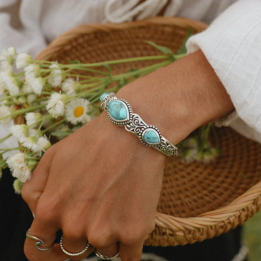 Woman in a white top carrying a basket of daisies wearing a large silver cuff with three turquoise stones on it.