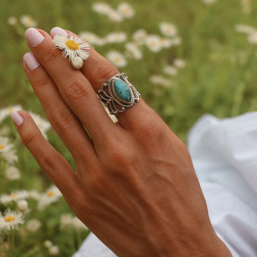 Woman's hand holding a daisy wearing a large sterling silver turquoise ring with silver vine detailing around the stone.