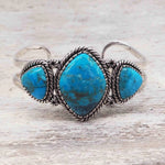 sterling silver large statement cuff with three natural Turquoise gemstones on a light wooden surface
