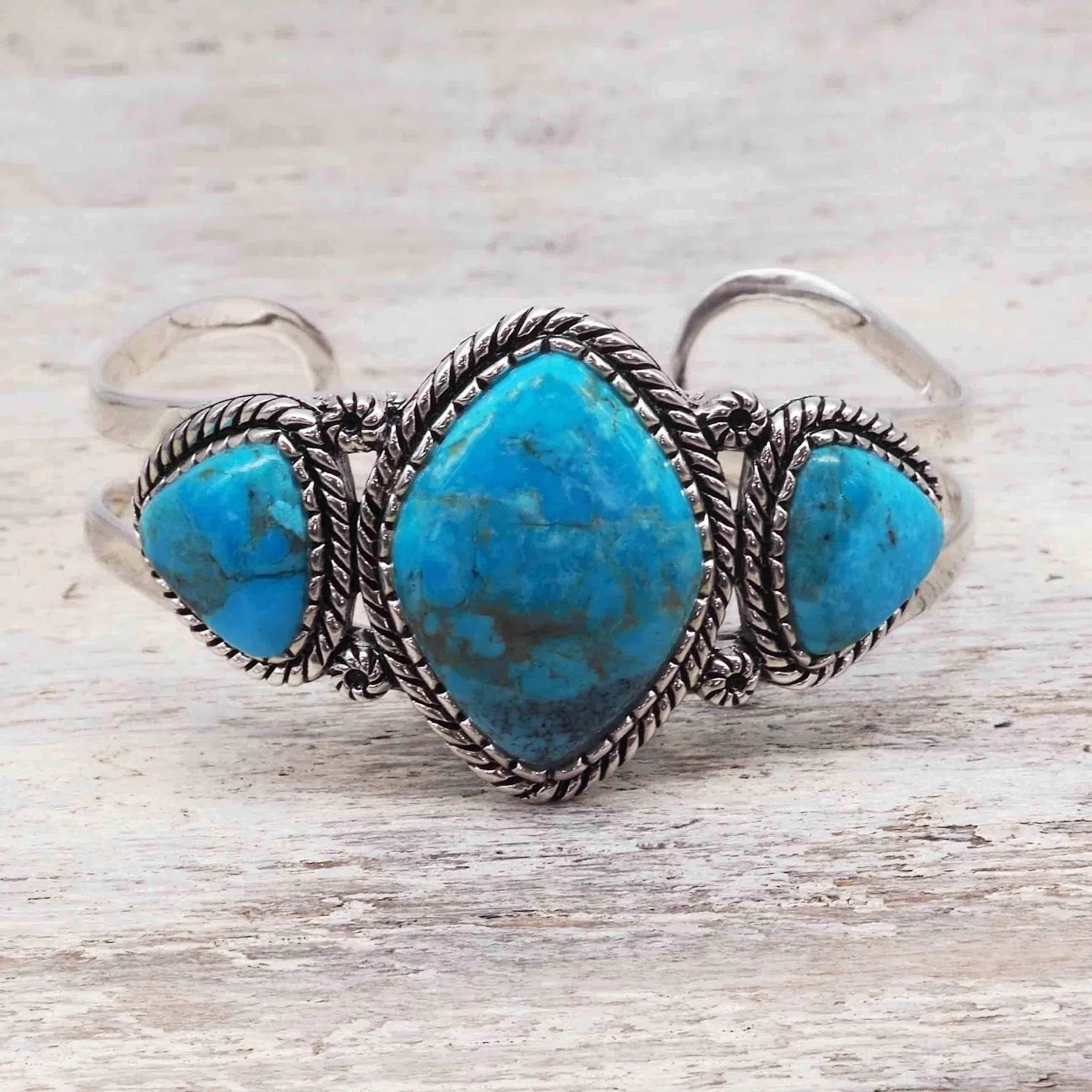 sterling silver large statement cuff with three natural Turquoise gemstones on a light wooden surface