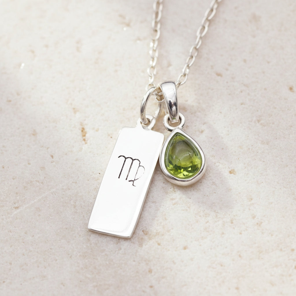 Necklace with a silver pendant featuring the Virgo zodiac sign and a green teardrop-shaped natural peridot charm on a textured background.