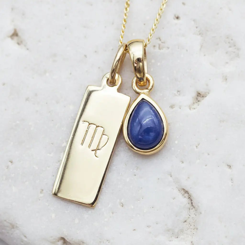 Gold necklace with Virgo zodiac sign pendant and September birthstone natural sapphire pendant on a textured background