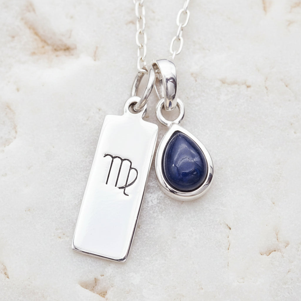 Silver necklace with virgo zodiac sign pendant and blue teardrop natural sapphire gemstone charm on a textured background