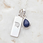 Silver necklace with virgo zodiac sign pendant and blue teardrop natural sapphire gemstone charm on a textured background