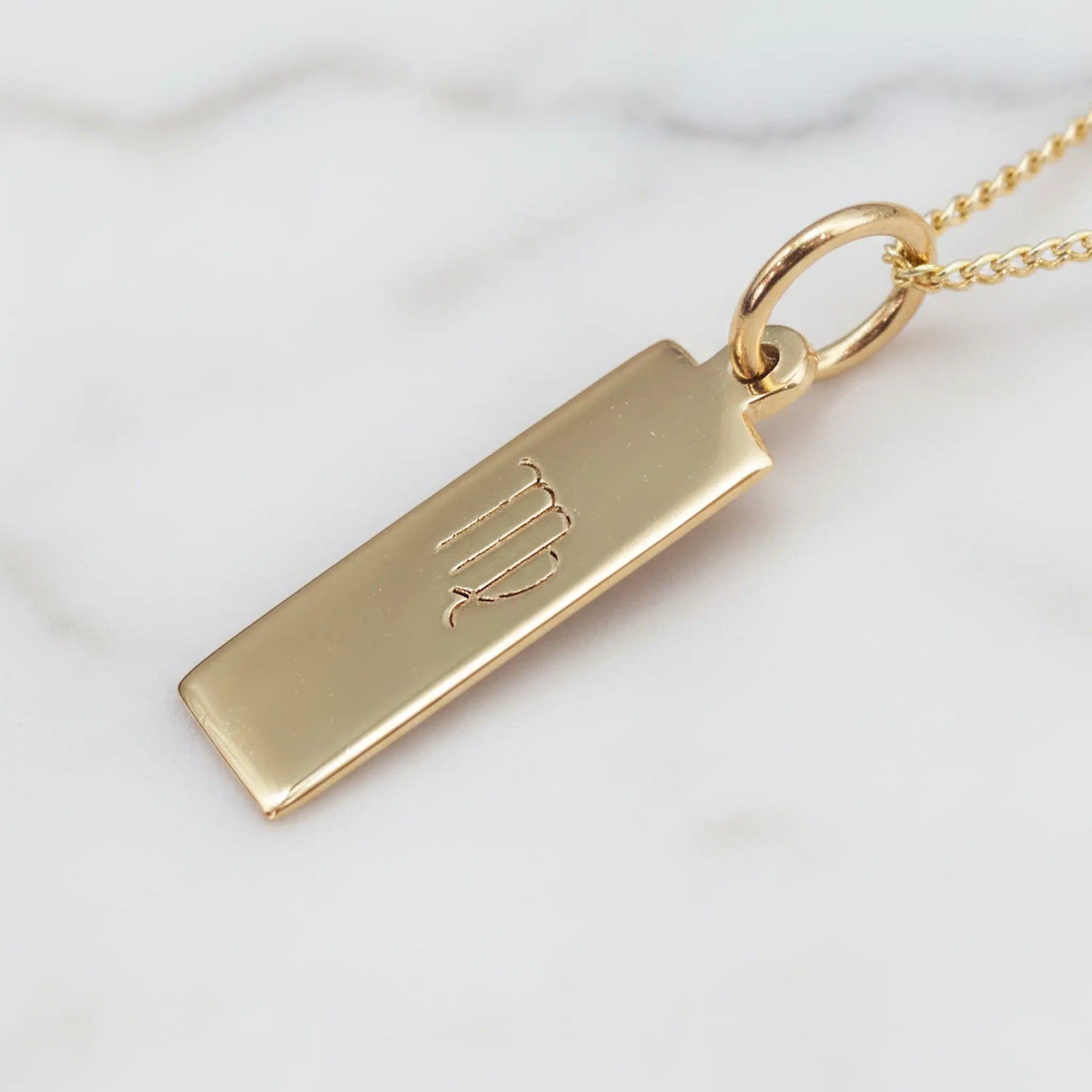 Gold pendant with virgo zodiac symbol on a white background