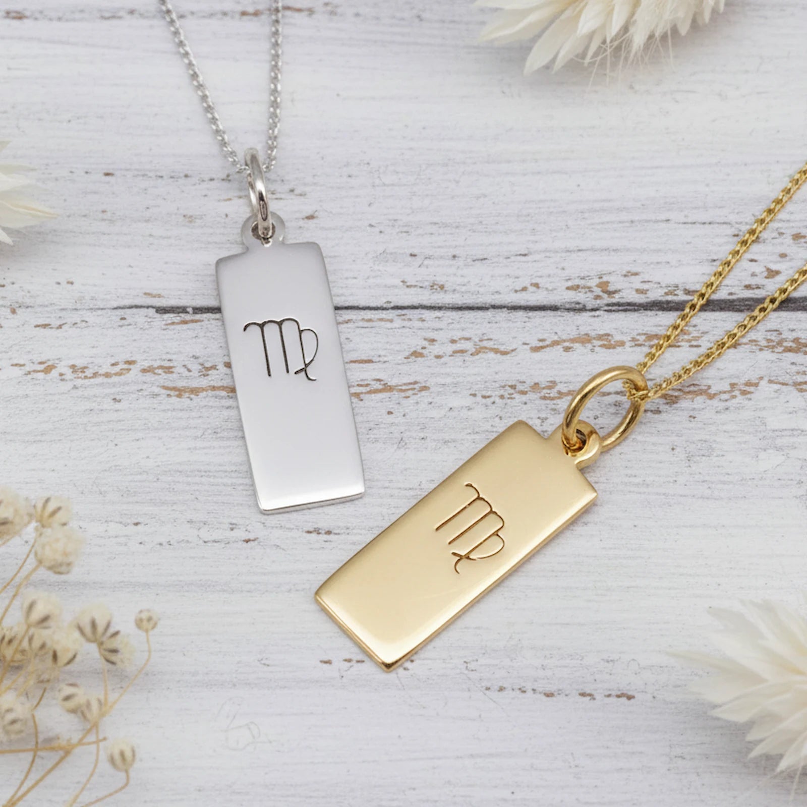 Gold-plated and sterling silver Virgo zodiac pendant necklaces with slim rectangular engraved glyph bar pendants on fine curb chains, displayed on a white wood surface.