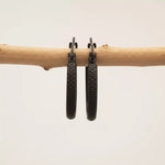 Black hoop earrings hanging on a branch against a beige background