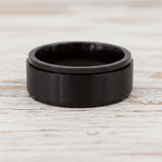 waterproof black spinner Ring in minimalist stainless steel band design on a light wooden surface