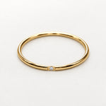 A thin yellow gold band ring with a single small clear gemstone set in the center, photographed on a clean white background.
