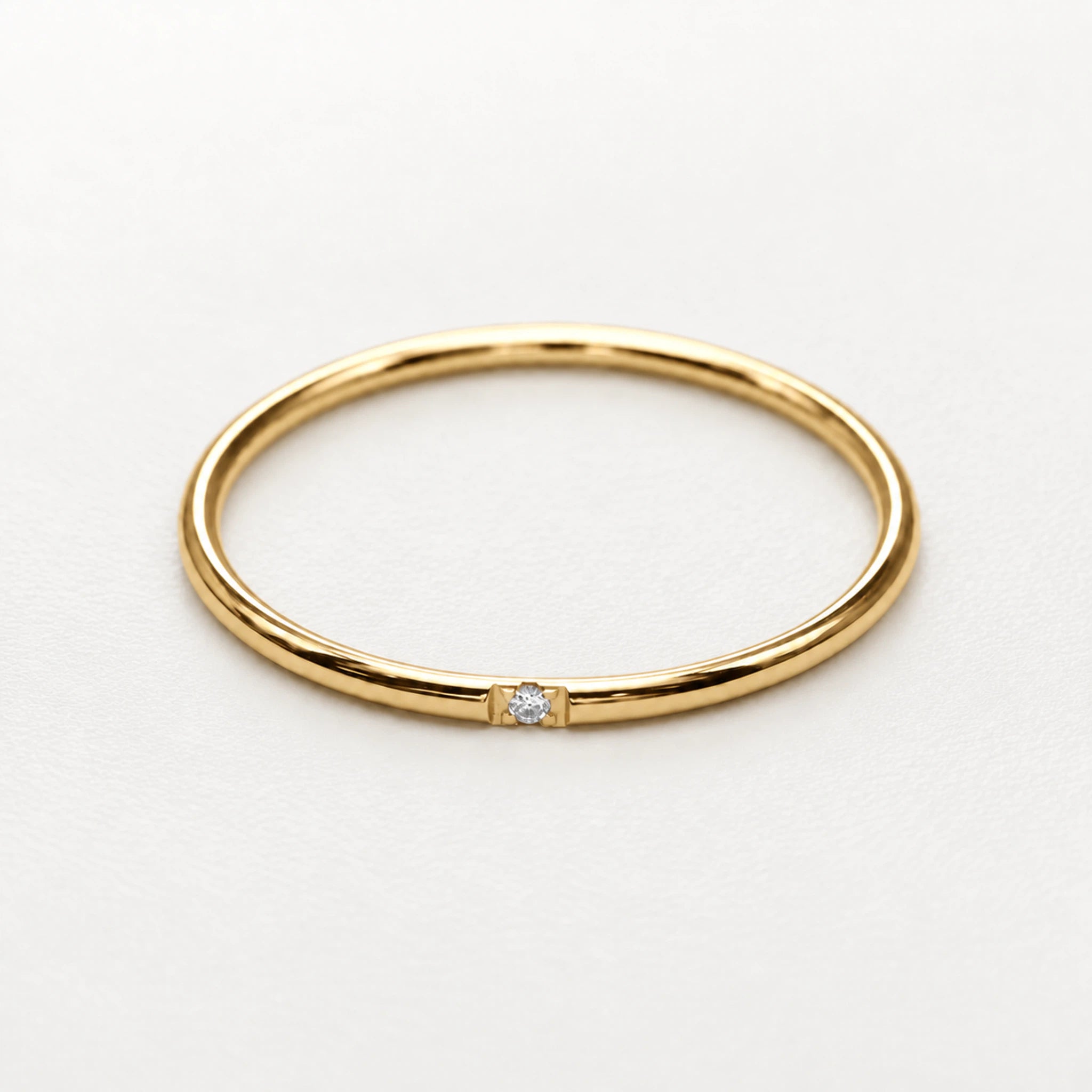 A thin yellow gold band ring with a single small clear gemstone set in the center, photographed on a clean white background.