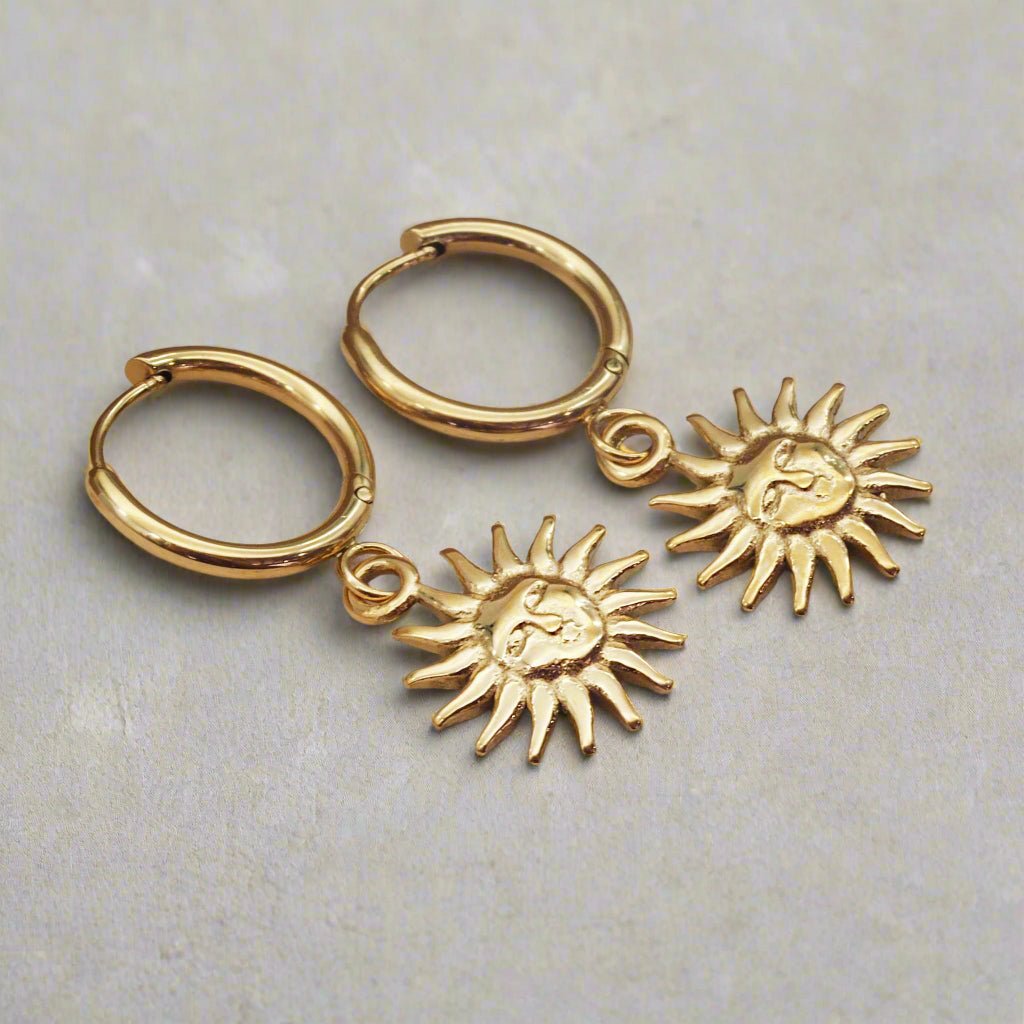 waterproof stainless steel sunburst char gold huggie earrings on a light grey surface