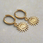 waterproof stainless steel sunburst char gold huggie earrings on a light grey surface