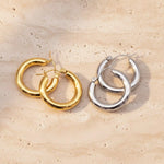 Gold and silver hoop earrings on a beige stone surface