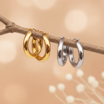 Two gold hoop earrings and two silver hoop earrings on a branch with a blurred background