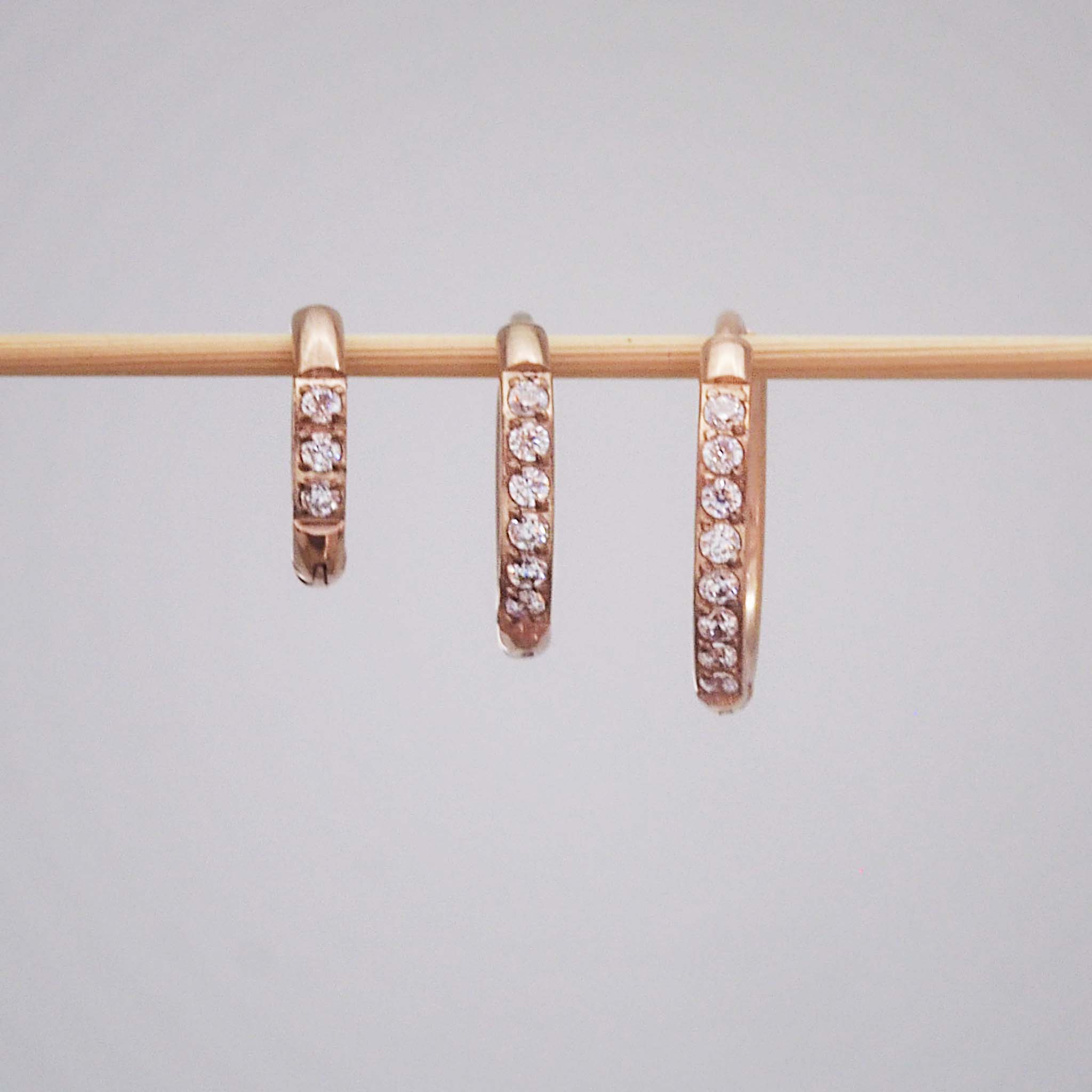 Three stainless steel waterproof pavé rose gold hoop earrings in three different hoop huggie earring sizes