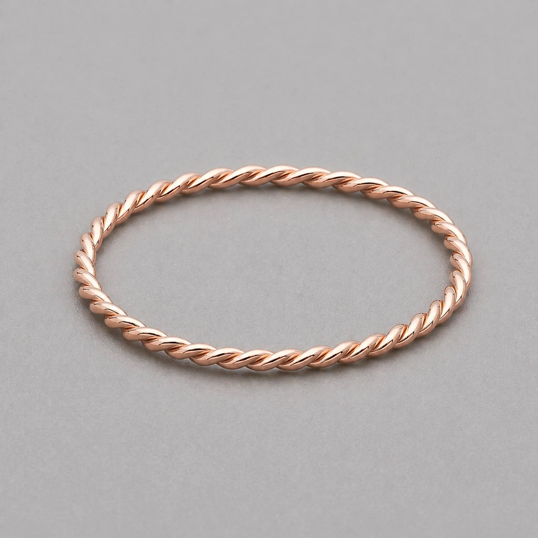 stainless steel waterproof rose gold twisted stacker ring on a grey surface