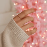 Hand wearing a stainless steel waterproof twisted rose gold stacker ring with a blurred pink light background 