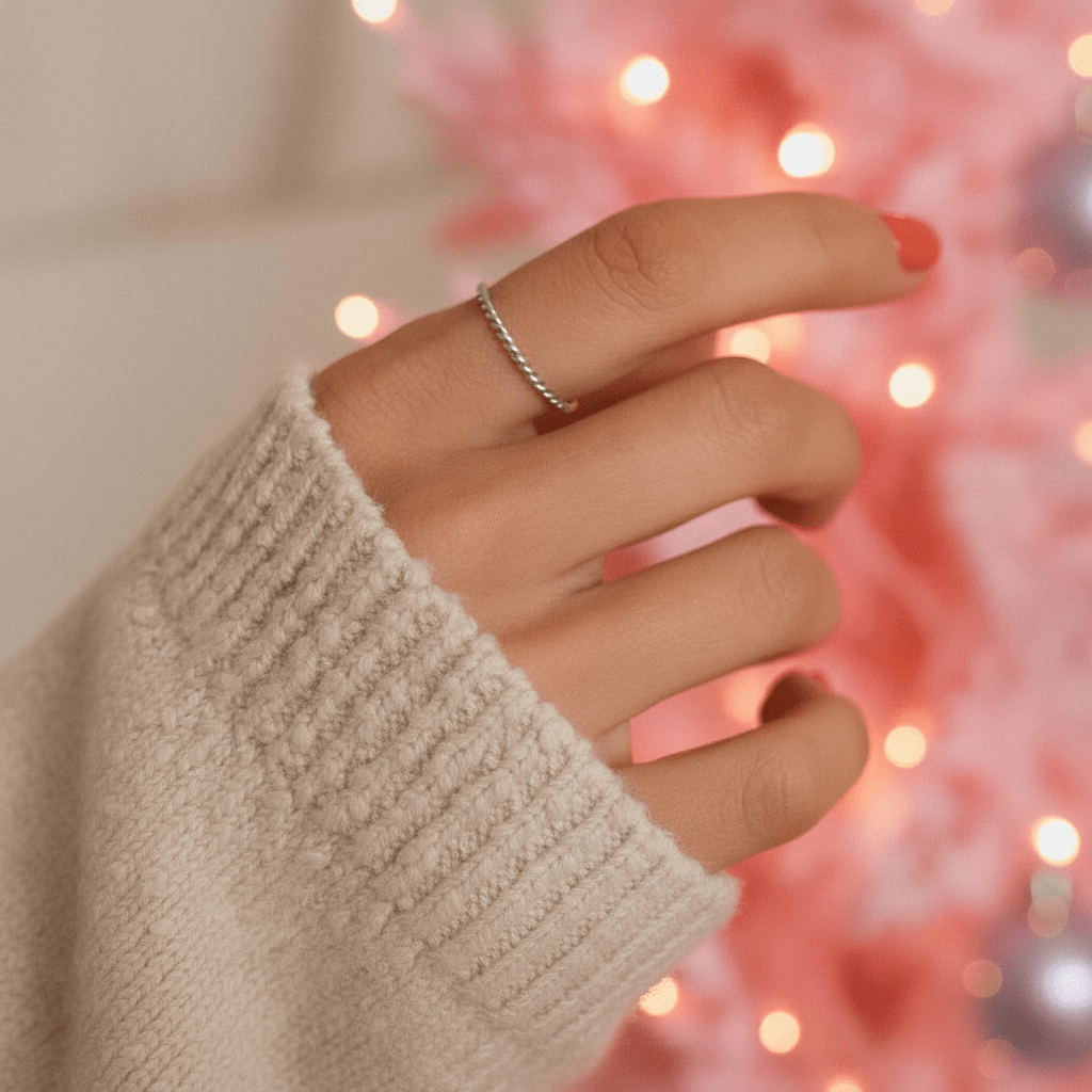 Hand wearing a stainlesss steel waterproof silver twisted stacker ring with a blurred festive background