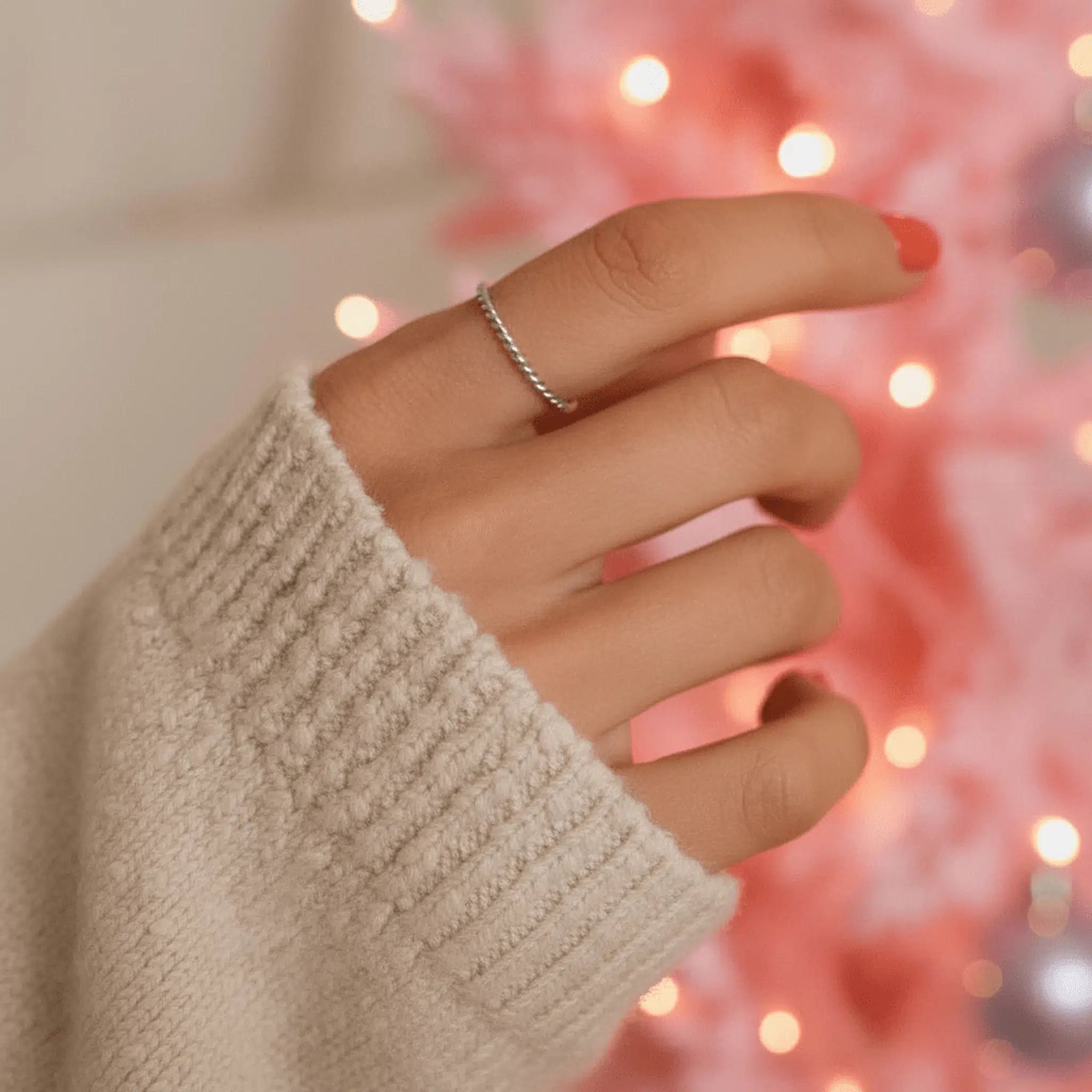 Hand wearing a stainlesss steel waterproof silver twisted stacker ring with a blurred festive background