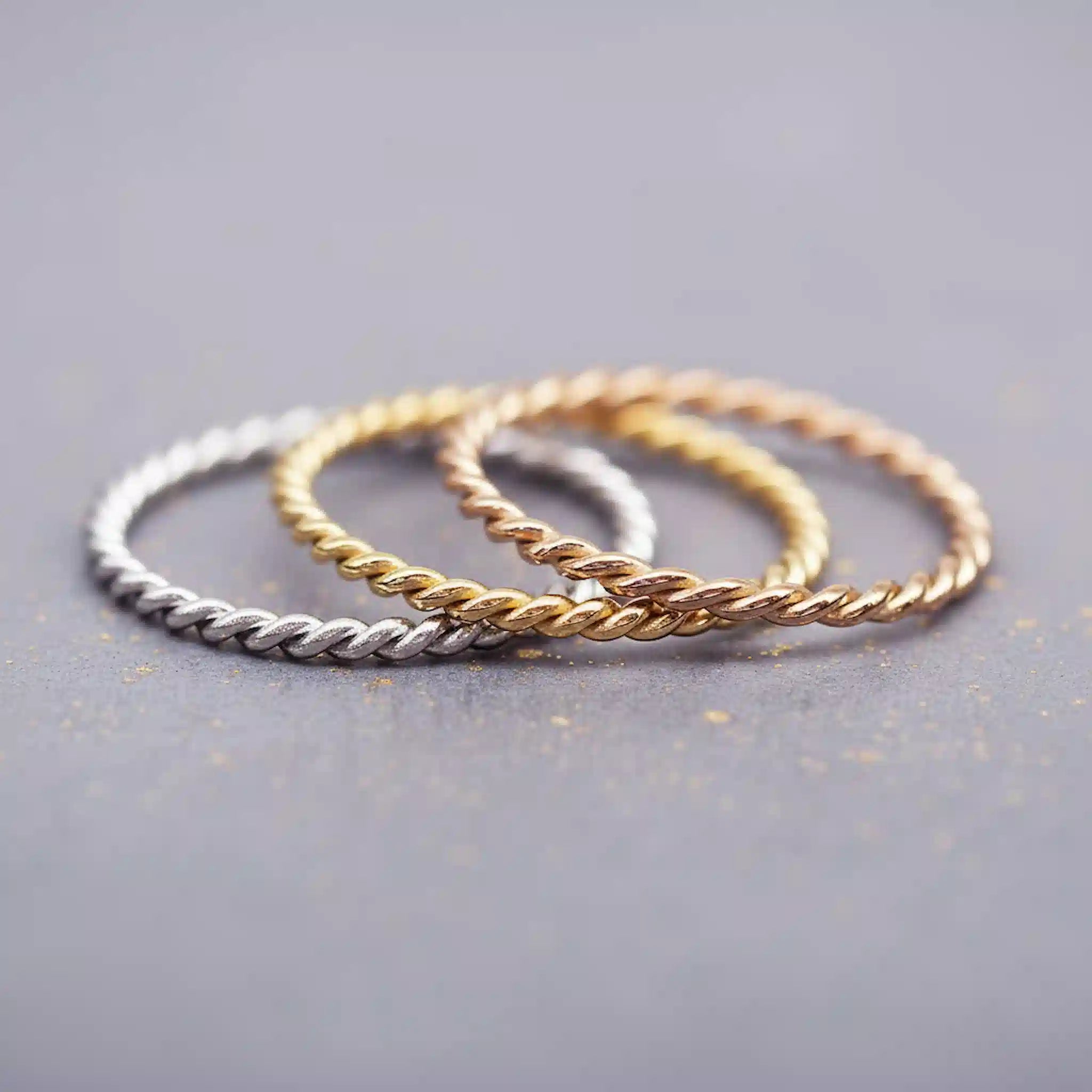 Waterproof twisted Stacker Rings in Silver, Gold and rose gold on a grey surface