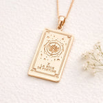 Rose Gold Wheel of Fortune tarot card pendant necklace on a white background with small flowers.