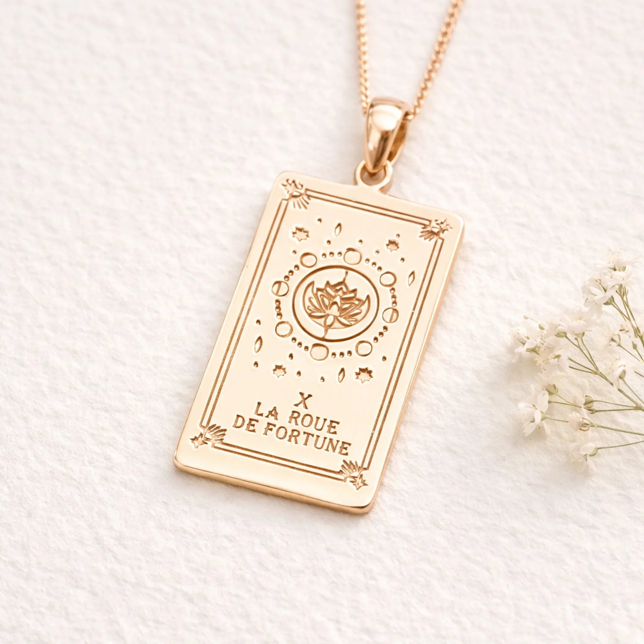 Rose Gold Wheel of Fortune tarot card pendant necklace on a white background with small flowers.