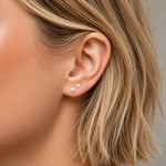 Close-up of an ear with white opal ball stud earrings and blonde hair.
