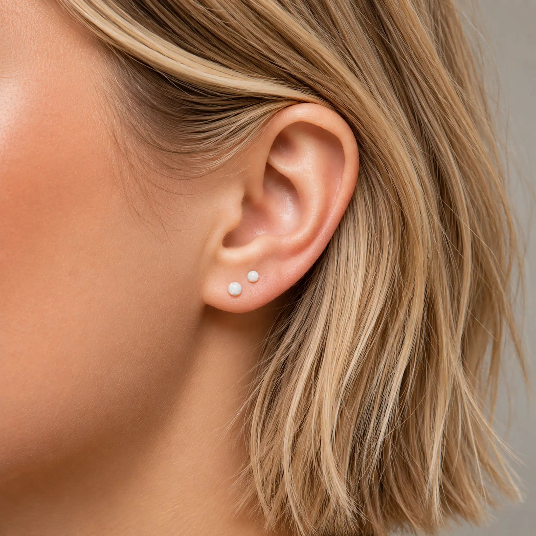 Close-up of an ear with white opal ball stud earrings and blonde hair.