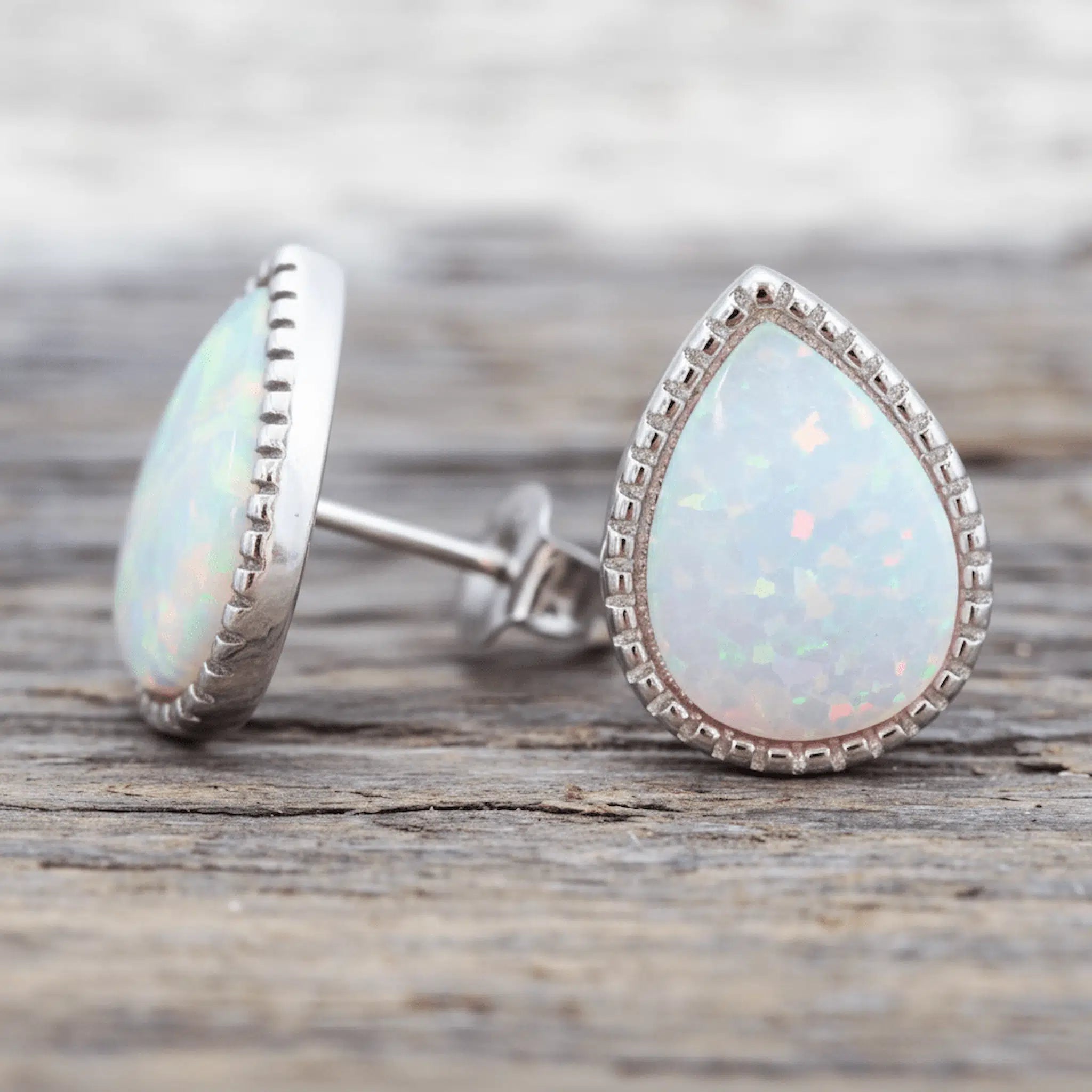 Teardrop-shaped opal earrings on a wooden surface
