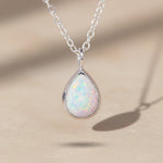 Teardrop-shaped white opal pendant on a silver chain against a gray background