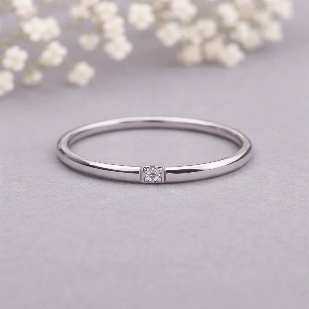Silver ring with a cz on a light gray background with white flowers.