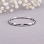 Silver ring with a cz on a light gray background with white flowers.