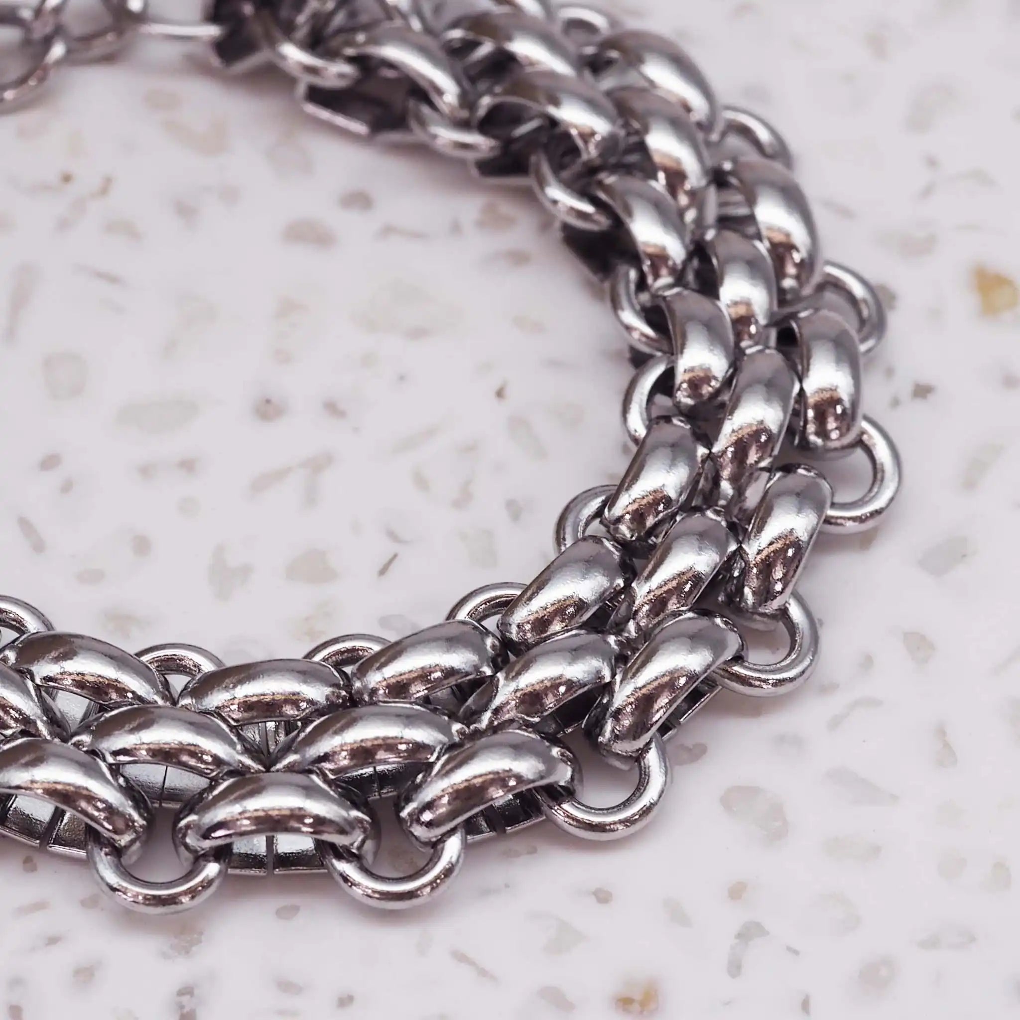 Close-up of silver chunky chain bracelet with shiny titanium links on a textured background. indie and harper