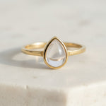 Gold ring with a clear herkimer quartz teardrop-shaped stone on a light background