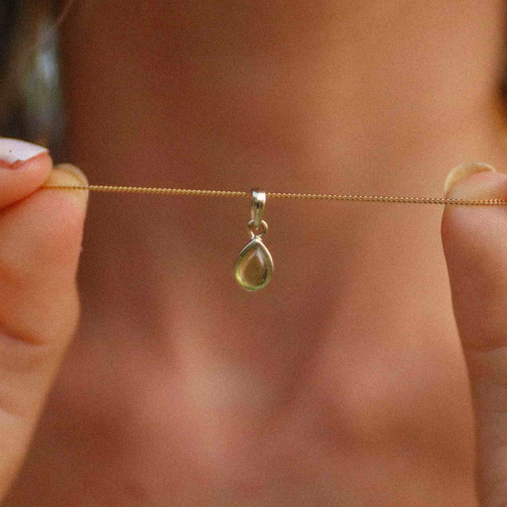 Gold August birthstone necklace with pear-shaped natural peridot gemstone pendant held - august birthstone jewellery gift for her