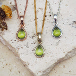 Three teardrop-shaped peridot stone pendants on silver, gold and rose gold chains against a white background.