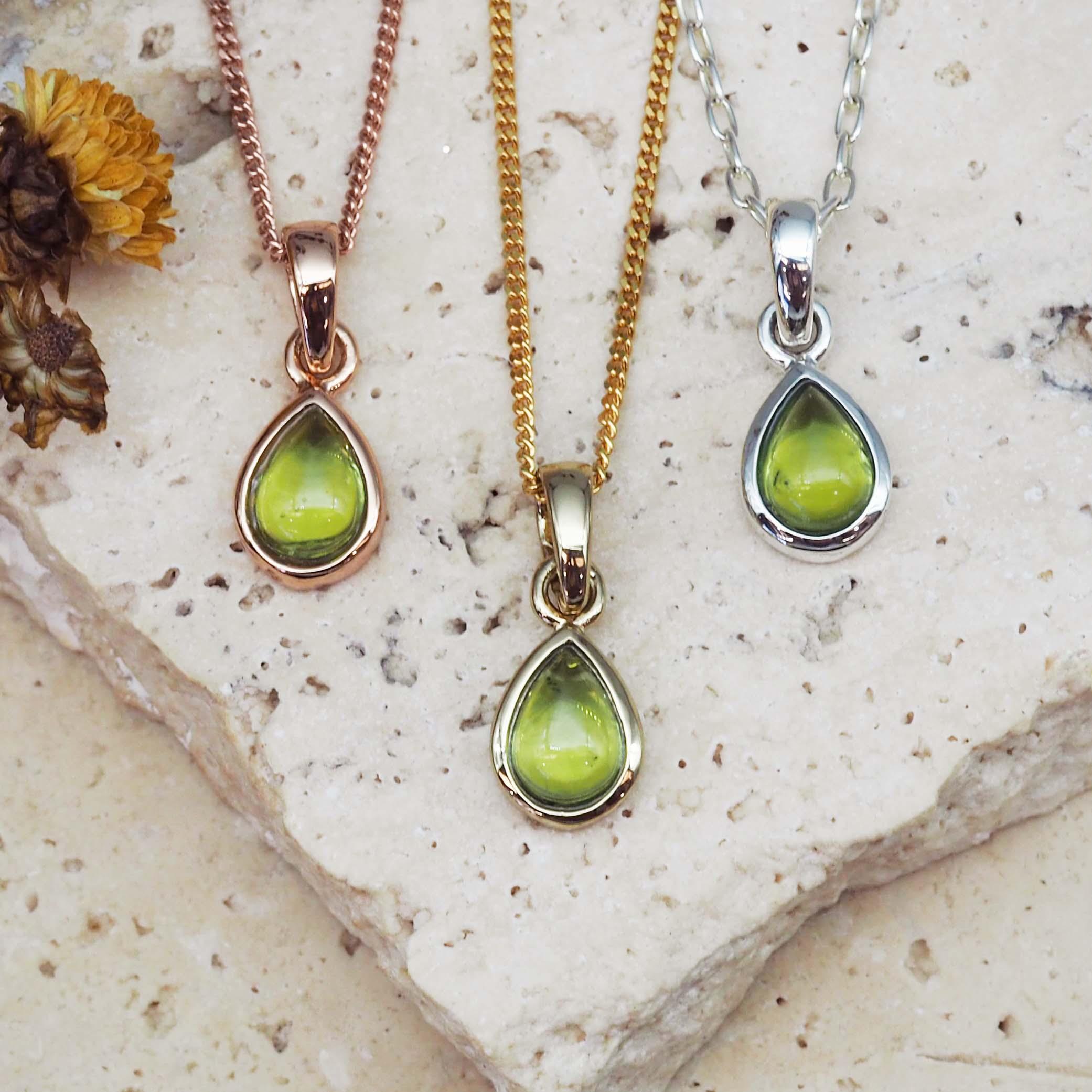 Three teardrop-shaped peridot stone pendants on silver, gold and rose gold chains against a white background.