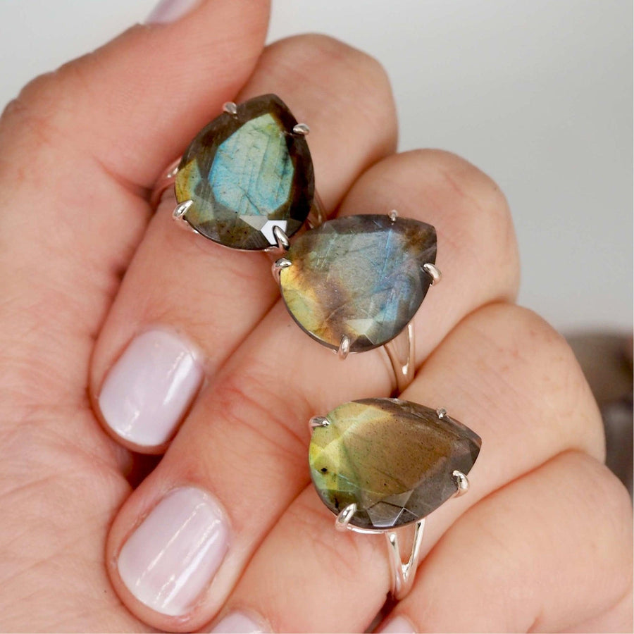fingers holding three different sterling silver rings with faceted labradorite gemstones