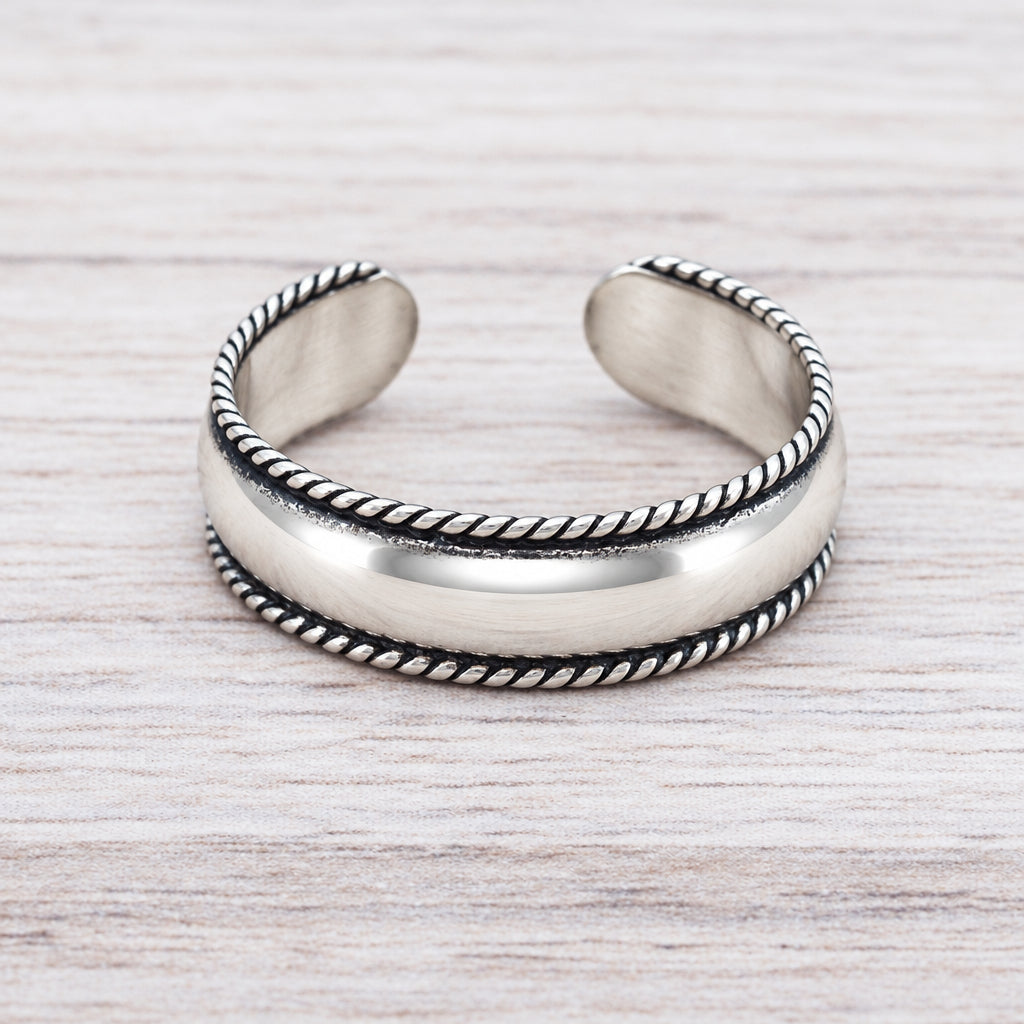 Sterling silver adjustable toe ring with a wide band and rope edge on a light wood surface