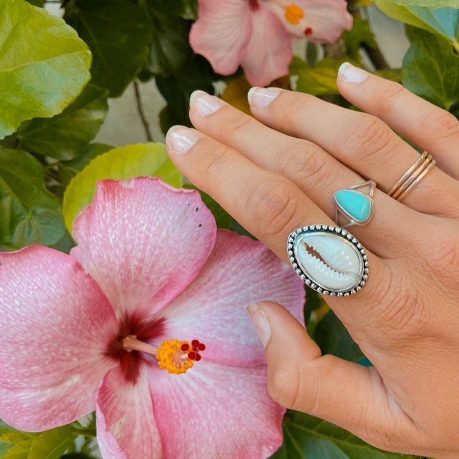 Hand wearing Cowrie Sea Shell Ring with pink flower and green leaves in the background - womens sterling silver jewellery Australia