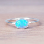 Dainty sterling silver ring with oval Blue Opal stone on a light wooden surface