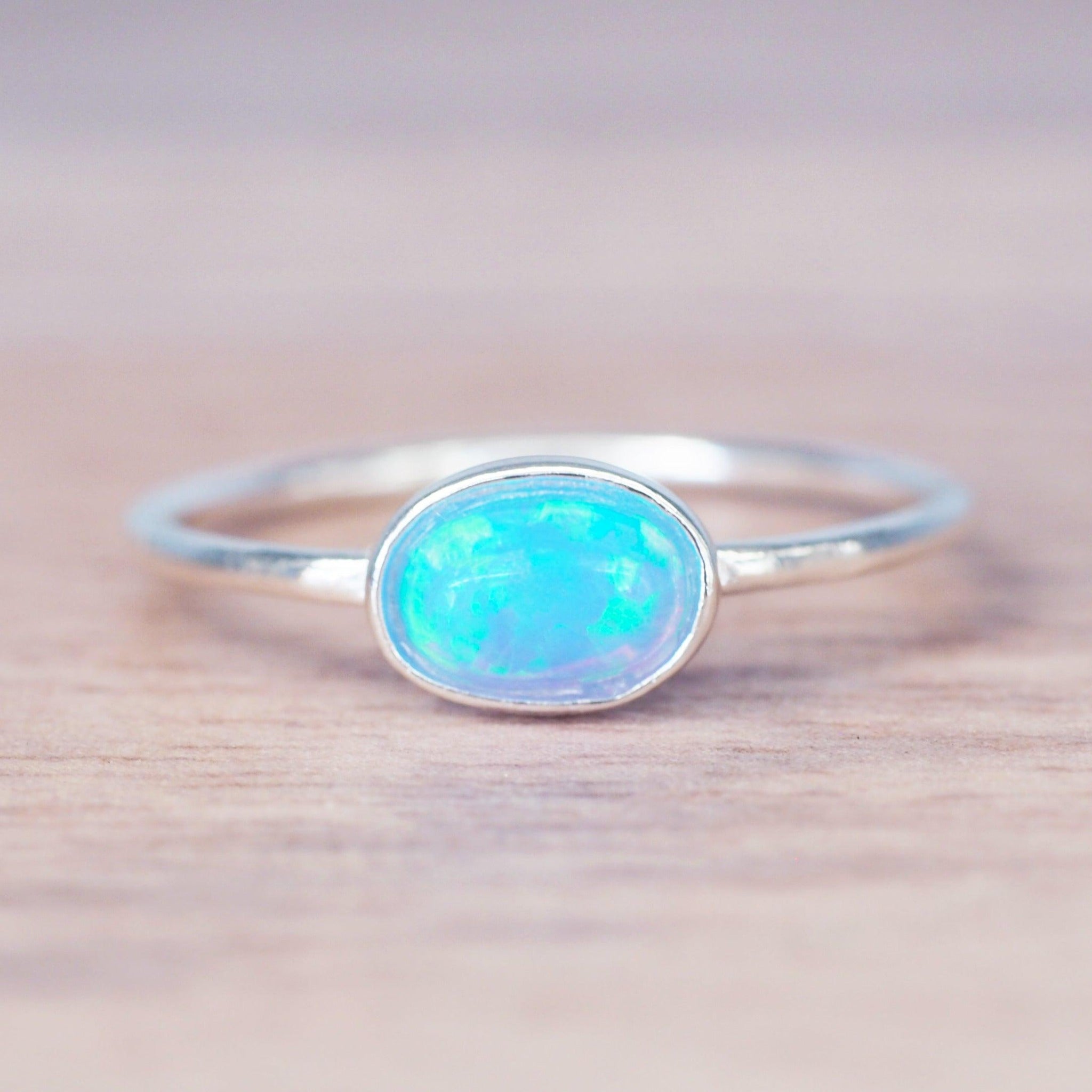 Dainty sterling silver ring with oval Blue Opal stone on a light wooden surface
