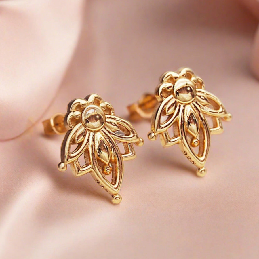 dainty gold earrings with lotus flower design sitting on light pink silk
